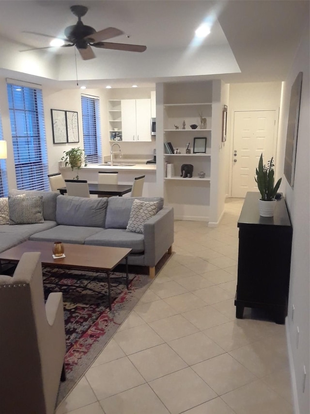 tiled living room featuring built in shelves, ceiling fan, and sink