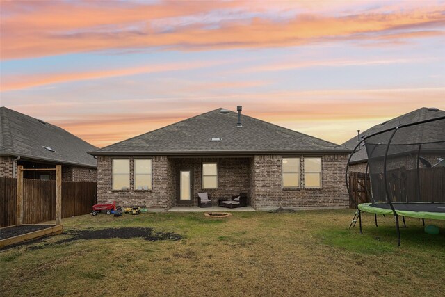 back house at dusk with a lawn, a patio, and a trampoline