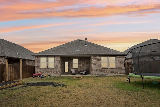 back house at dusk featuring a trampoline, a patio area, and a lawn