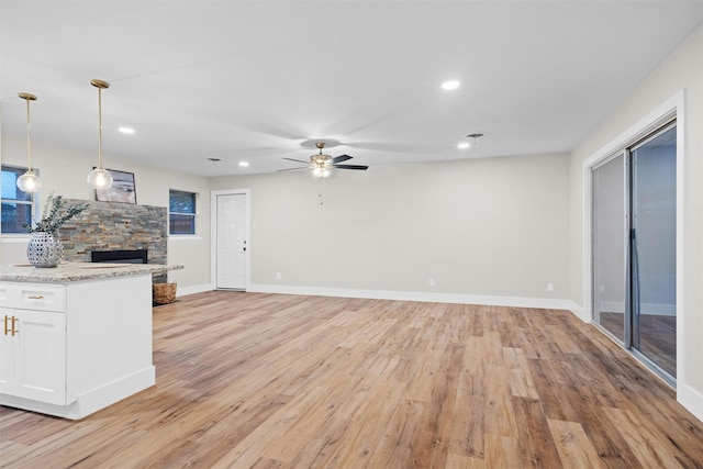 kitchen featuring white cabinets, hanging light fixtures, light hardwood / wood-style flooring, ceiling fan, and light stone countertops