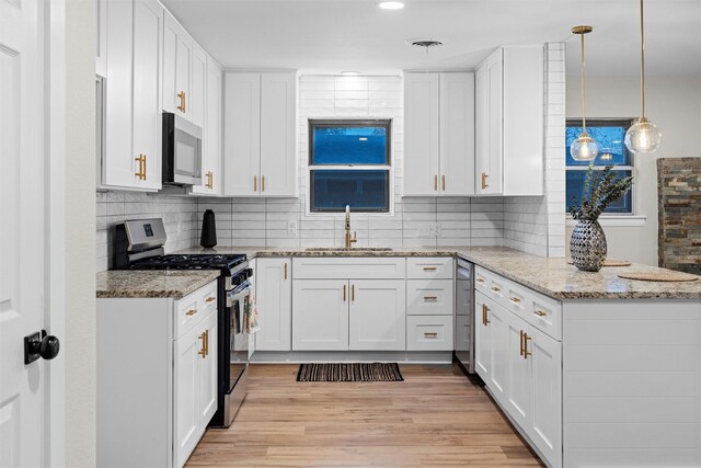 kitchen with appliances with stainless steel finishes, sink, pendant lighting, white cabinets, and light hardwood / wood-style floors