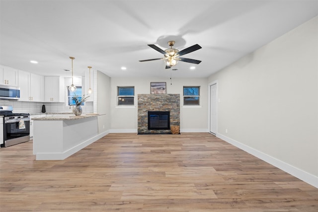 unfurnished living room with ceiling fan, a stone fireplace, and light wood-type flooring