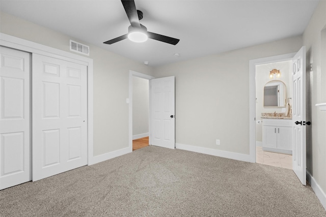 unfurnished bedroom with light colored carpet, ensuite bath, a closet, and ceiling fan