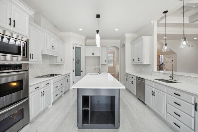 kitchen with ceiling fan, stainless steel appliances, coffered ceiling, decorative light fixtures, and a kitchen island with sink