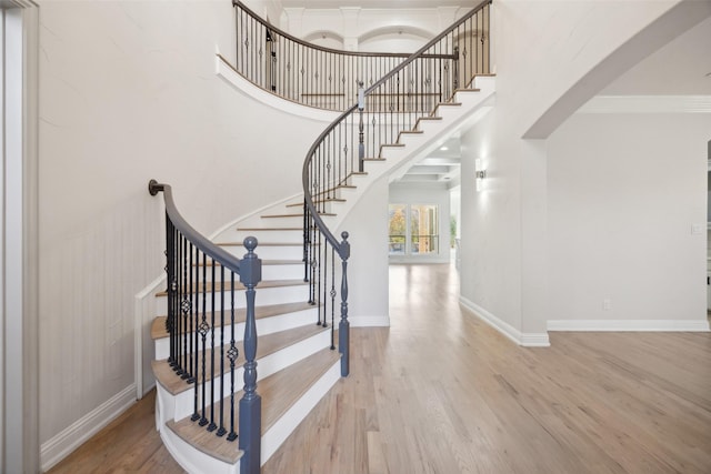 stairs featuring ornamental molding, a high ceiling, baseboards, and wood finished floors