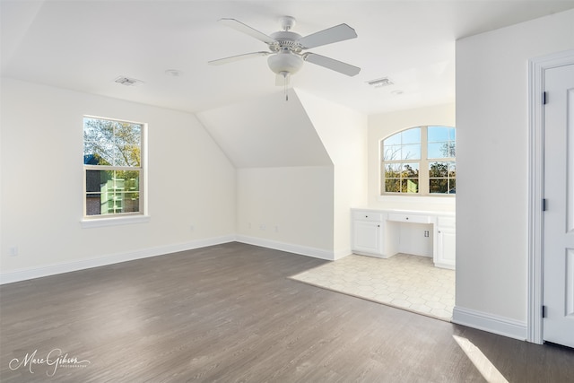 bonus room with lofted ceiling, dark hardwood / wood-style floors, built in desk, and ceiling fan