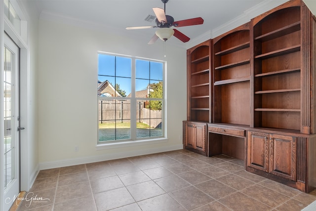 unfurnished office featuring ceiling fan, light tile patterned floors, built in desk, and crown molding