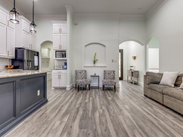 living room featuring a towering ceiling, light wood-type flooring, and ornamental molding