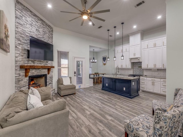 living room with ceiling fan with notable chandelier, crown molding, sink, a fireplace, and light hardwood / wood-style floors