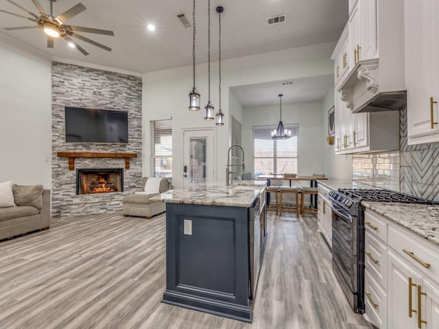 kitchen featuring a center island with sink, decorative light fixtures, gas stove, and light stone counters