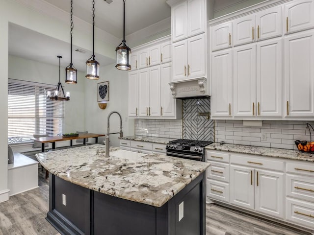 kitchen with backsplash, high end black range, a kitchen island with sink, white cabinets, and decorative light fixtures