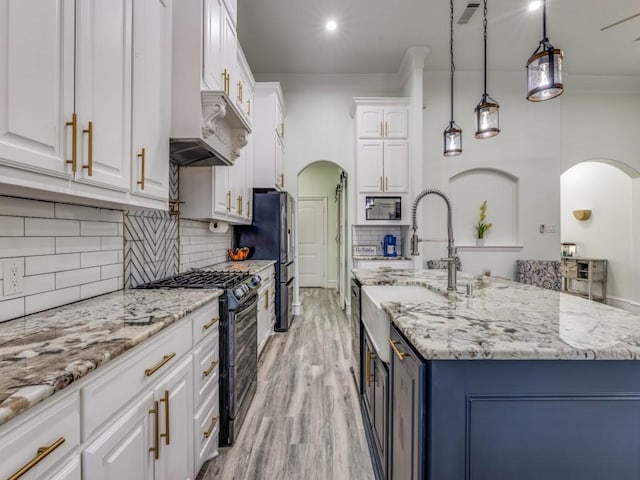 kitchen featuring a kitchen island with sink, black appliances, hanging light fixtures, light stone counters, and white cabinetry