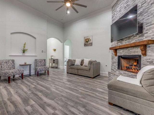 living room featuring a stone fireplace, ceiling fan, ornamental molding, a towering ceiling, and wood-type flooring