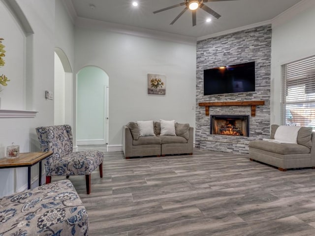 living room with ceiling fan, a stone fireplace, ornamental molding, and light hardwood / wood-style flooring