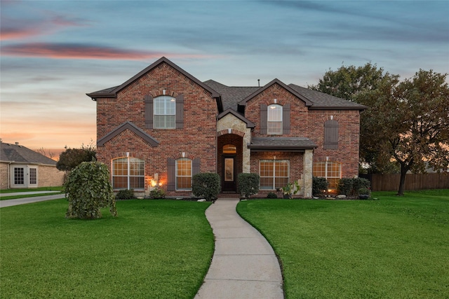 traditional-style home featuring brick siding, a front yard, fence, and a shingled roof