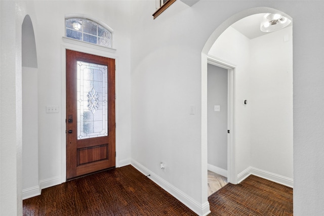 entrance foyer featuring arched walkways, baseboards, and wood finished floors