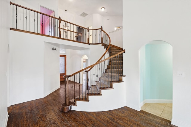 staircase with arched walkways, a high ceiling, wood finished floors, visible vents, and baseboards