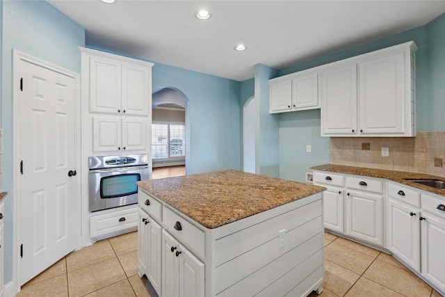 kitchen featuring stainless steel oven, white cabinets, dark stone counters, and a kitchen island