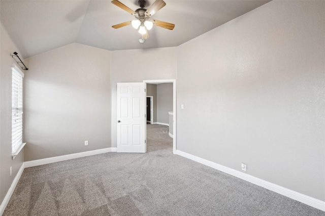 carpeted empty room featuring baseboards, vaulted ceiling, and a ceiling fan