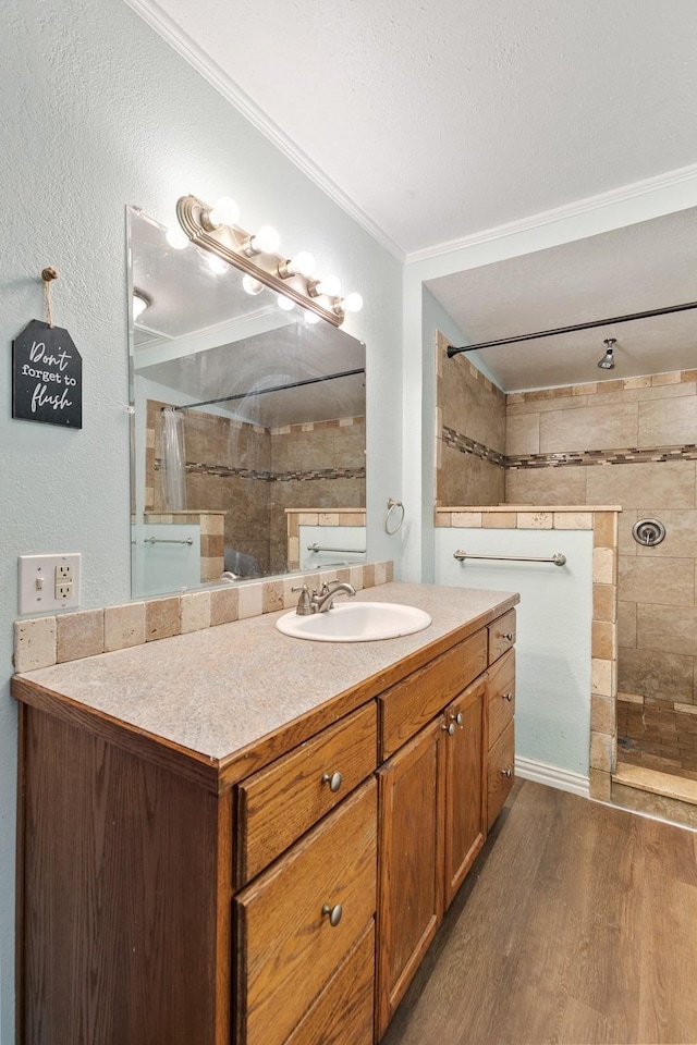 bathroom featuring hardwood / wood-style flooring, tiled shower, vanity, and ornamental molding