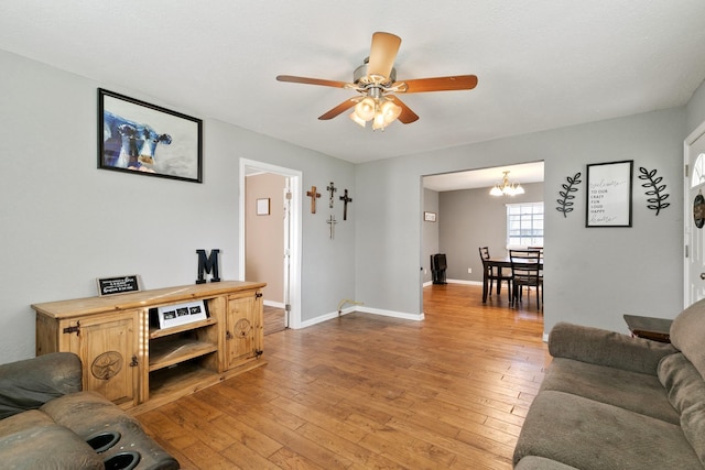 living room featuring ceiling fan with notable chandelier and light wood-type flooring