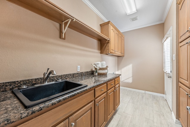 kitchen with ornamental molding, sink, light hardwood / wood-style flooring, and dark stone countertops