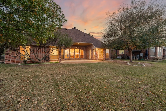 back house at dusk featuring a yard and a patio area