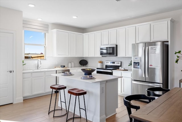 kitchen with white cabinetry, sink, a center island, stainless steel appliances, and light hardwood / wood-style floors