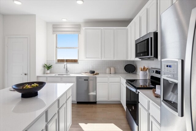 kitchen with appliances with stainless steel finishes, tasteful backsplash, sink, light hardwood / wood-style flooring, and white cabinets