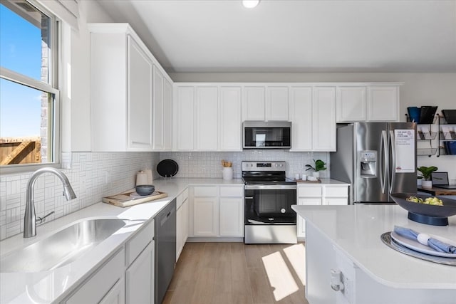 kitchen with sink, light hardwood / wood-style flooring, backsplash, white cabinets, and appliances with stainless steel finishes