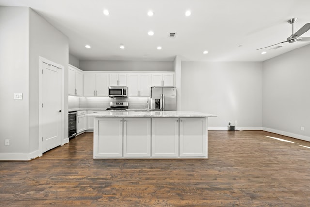 kitchen featuring light stone counters, a center island with sink, white cabinets, and stainless steel appliances