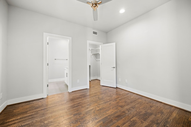 unfurnished bedroom featuring ceiling fan, dark hardwood / wood-style flooring, a walk in closet, and a closet