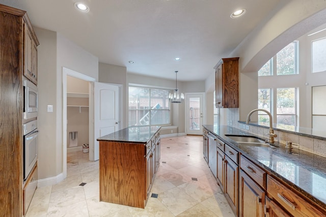 kitchen featuring appliances with stainless steel finishes, sink, decorative light fixtures, dark stone countertops, and a kitchen island