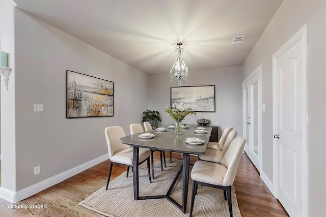 dining space with visible vents, a notable chandelier, baseboards, and wood finished floors