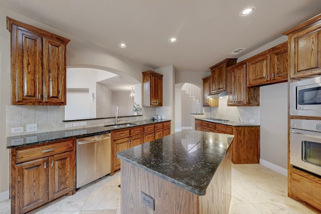 kitchen featuring sink, tasteful backsplash, dark stone countertops, a kitchen island, and appliances with stainless steel finishes