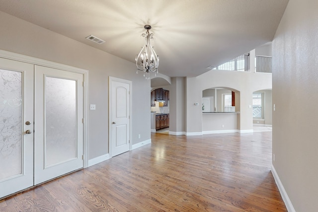 interior space with arched walkways, a notable chandelier, wood finished floors, visible vents, and baseboards