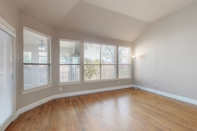 spare room featuring lofted ceiling, light wood-style flooring, and baseboards