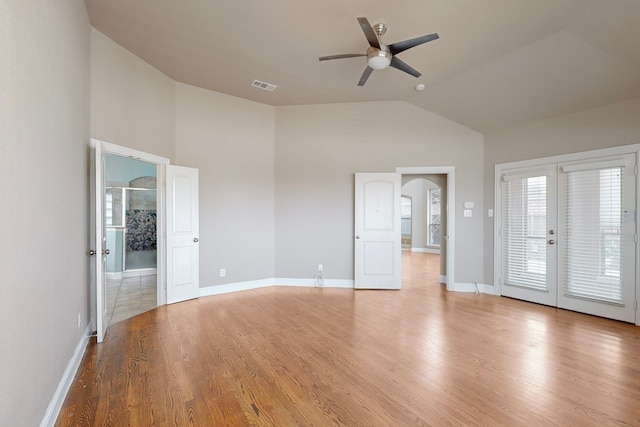 unfurnished bedroom with arched walkways, light wood finished floors, visible vents, high vaulted ceiling, and baseboards