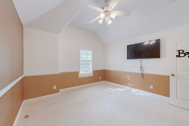 interior space featuring light carpet, a wainscoted wall, vaulted ceiling, and a ceiling fan