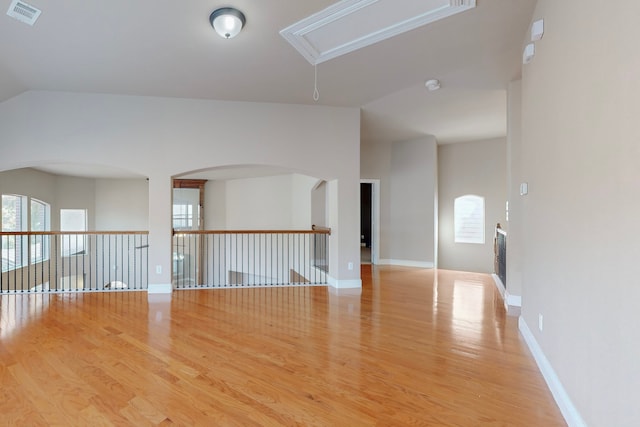 empty room featuring light wood-style floors, attic access, visible vents, and vaulted ceiling