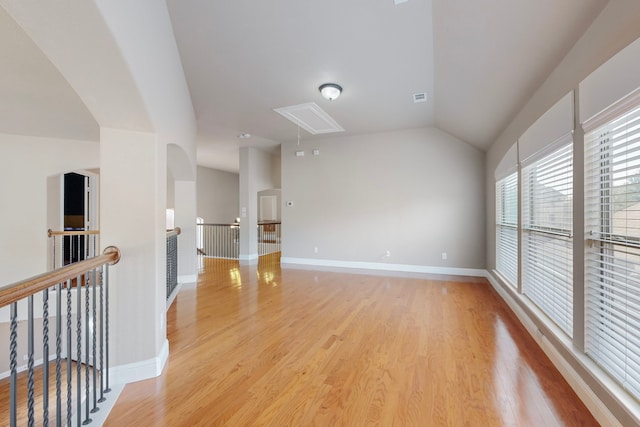 spare room with lofted ceiling, light wood-style flooring, attic access, and baseboards