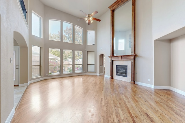 unfurnished living room with ceiling fan, light hardwood / wood-style flooring, a towering ceiling, and a healthy amount of sunlight