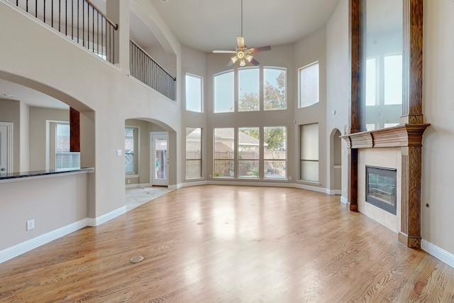 unfurnished living room with a tile fireplace, ceiling fan, light hardwood / wood-style flooring, and a towering ceiling