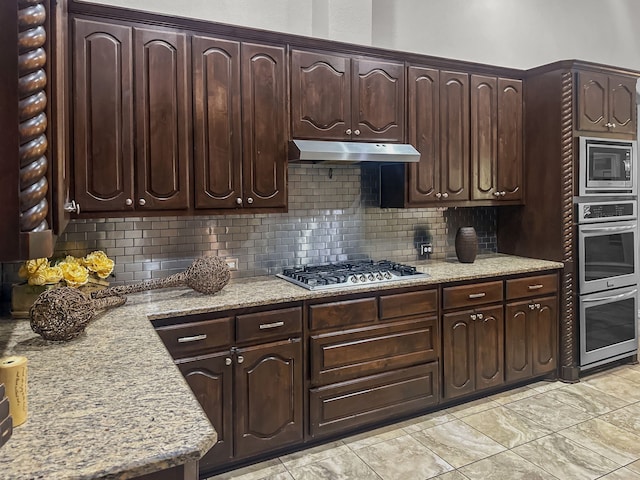 kitchen featuring dark brown cabinetry, appliances with stainless steel finishes, light stone countertops, and backsplash