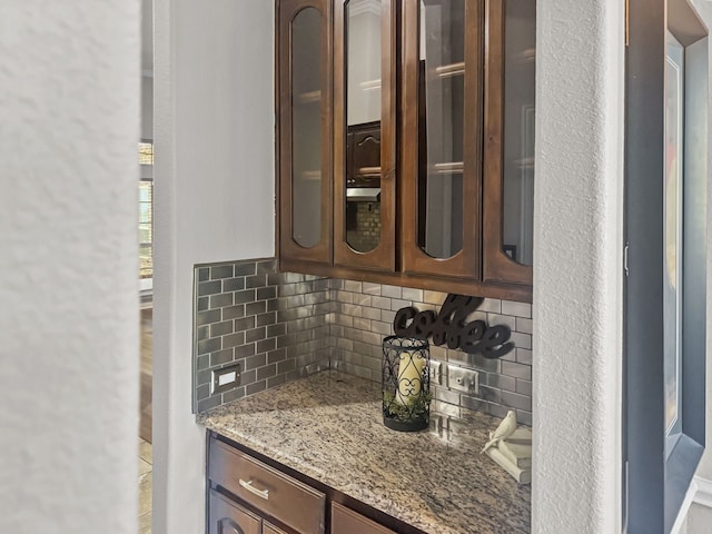 interior space with light stone counters, dark brown cabinets, and backsplash