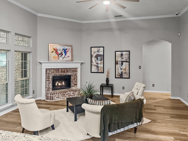 living room with crown molding, a brick fireplace, wood-type flooring, and ceiling fan