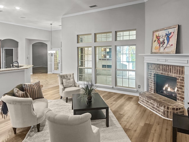 living room with a towering ceiling, ornamental molding, a fireplace, and light hardwood / wood-style flooring