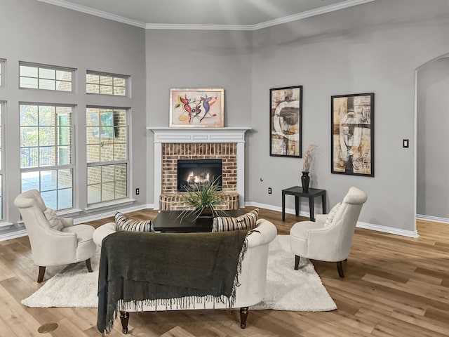 living area with hardwood / wood-style flooring, ornamental molding, and a brick fireplace