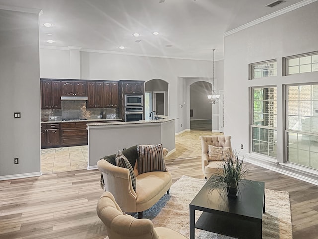 living room featuring crown molding, sink, an inviting chandelier, and light wood-type flooring