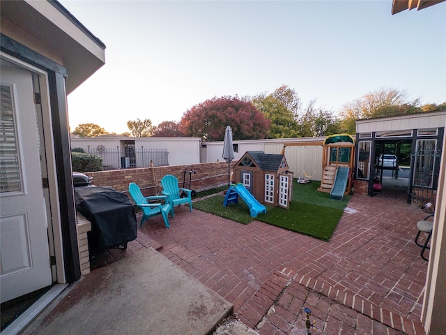 patio terrace at dusk with a playground, area for grilling, and a storage shed